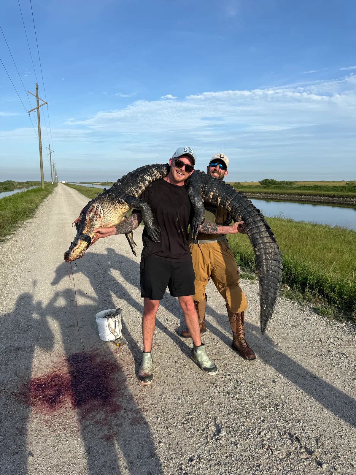 Two Florida hunters carrying a harvested alligator over their shoulders beside a canal